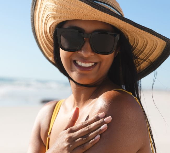 Smiling woman with sunglasses at the beach caressing her shoulder