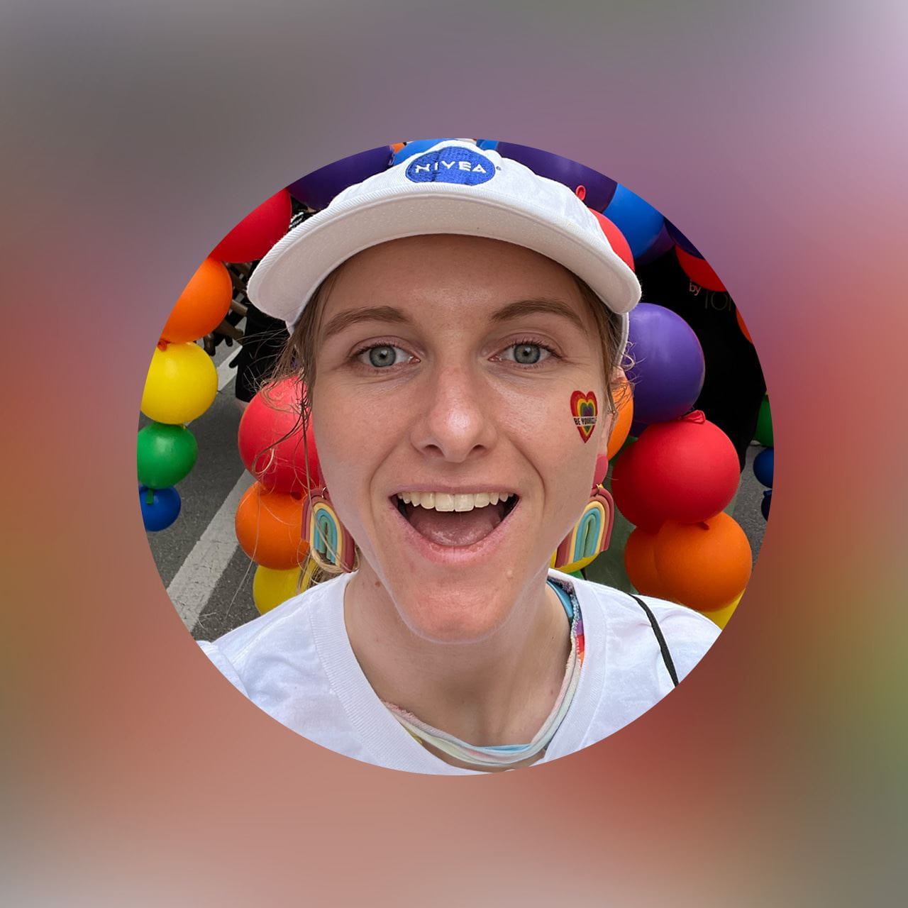 A selfie of a smiling woman in a white cap and shirt in front of a rainbow display.