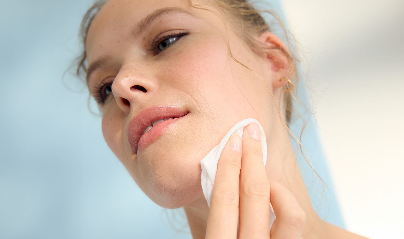 A view of a person rubbing a soft, white towelette onto the left side of their face.