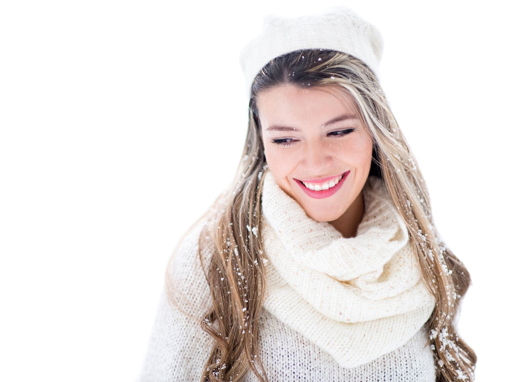 View of a female model wearing a white hat and scarf and a grey sweater while smiling against a white background.