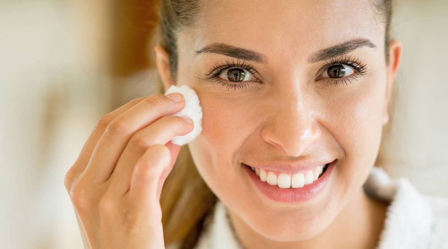 brunette lady using lactic acid skin on her face with a cotton pad
