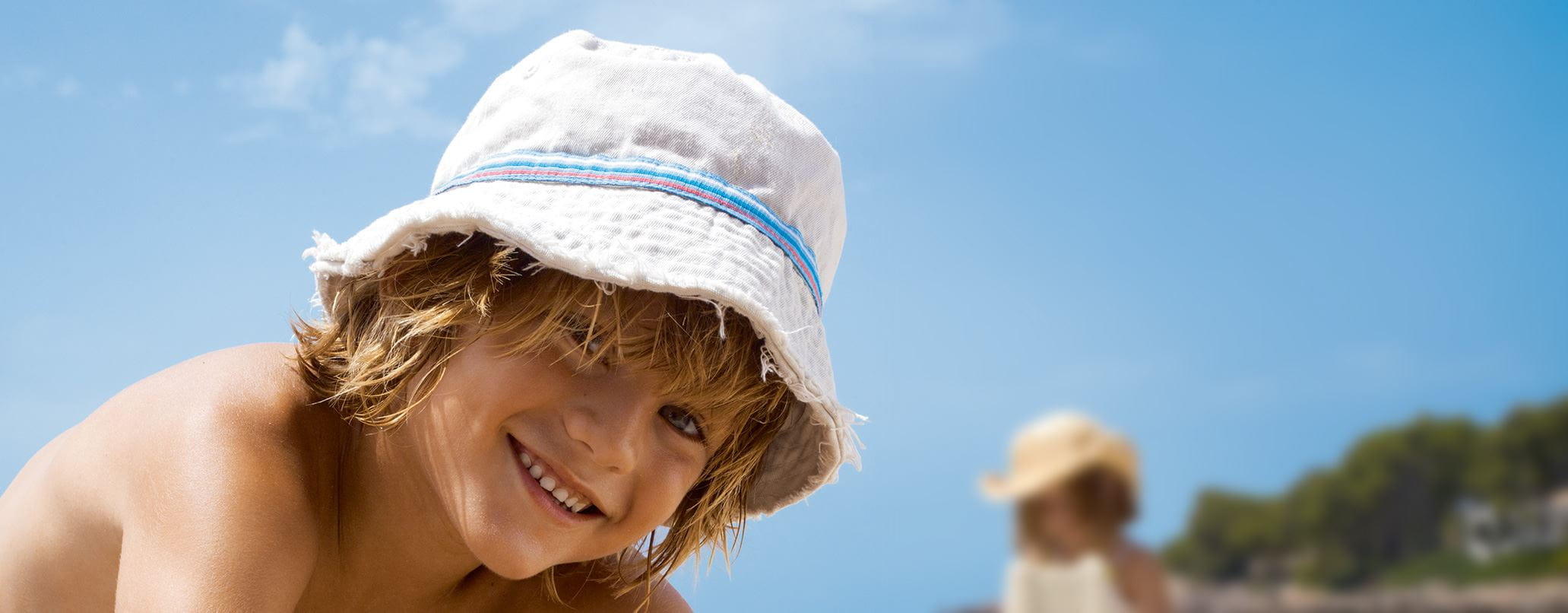 criança de chapéu a brincar na praia