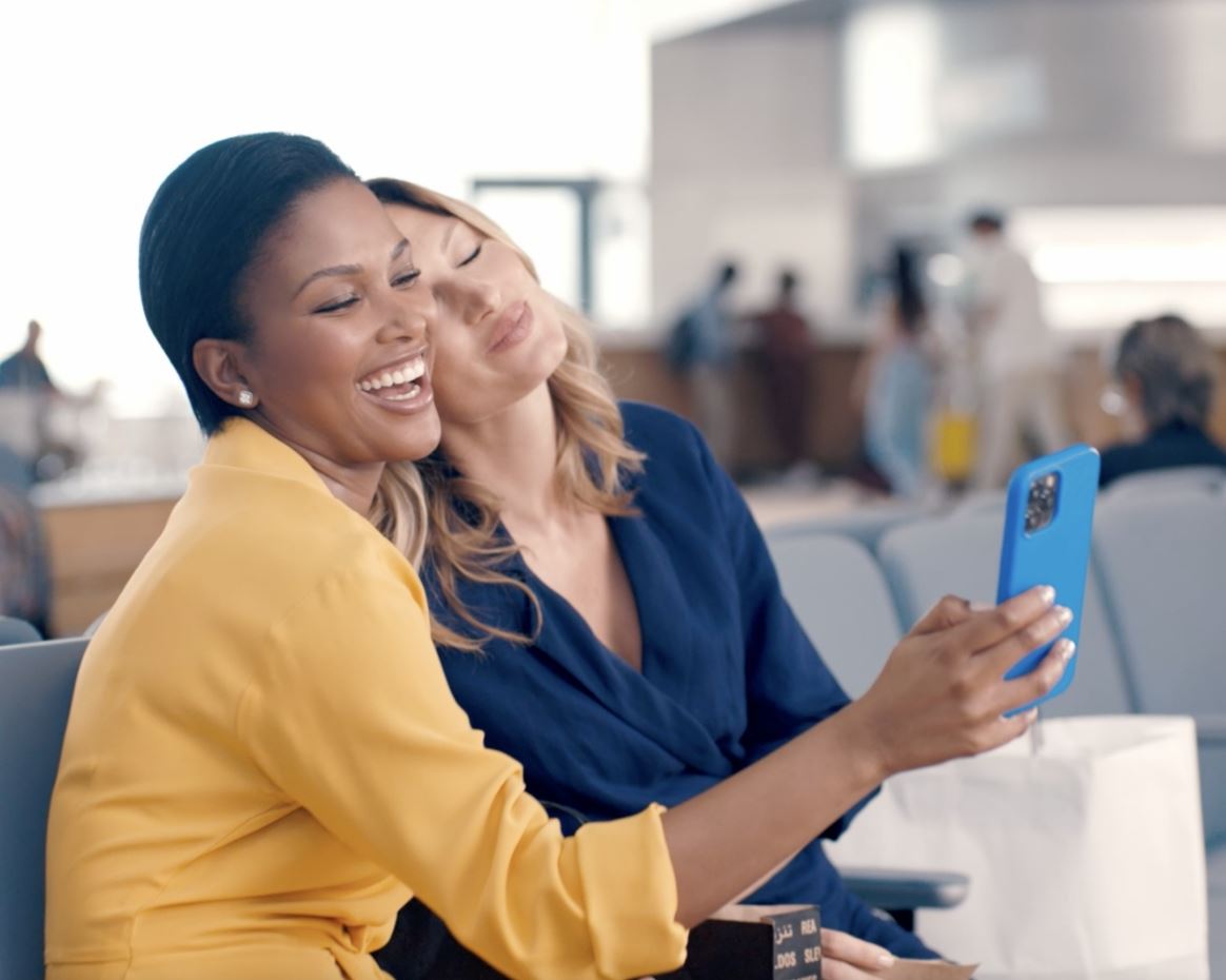 View of two female models smiling while holding a cell phone.
