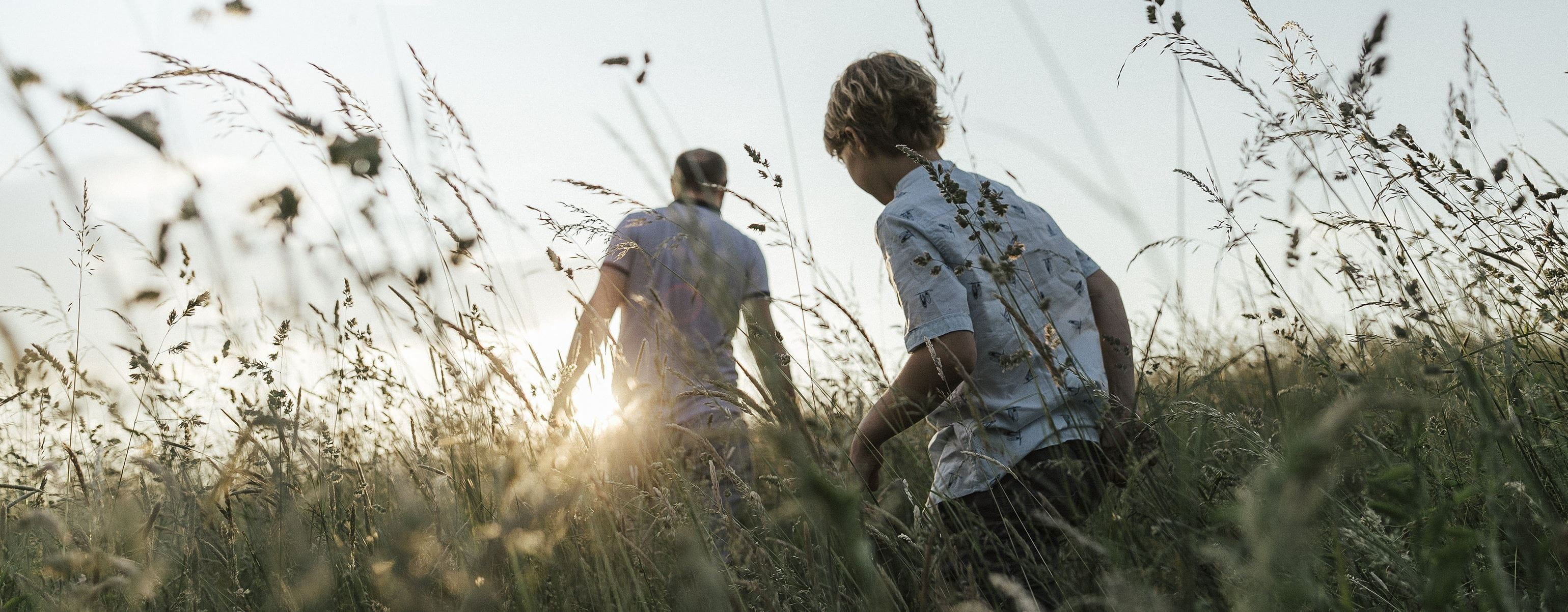 pai e filho a caminhar num campo com plantas secas