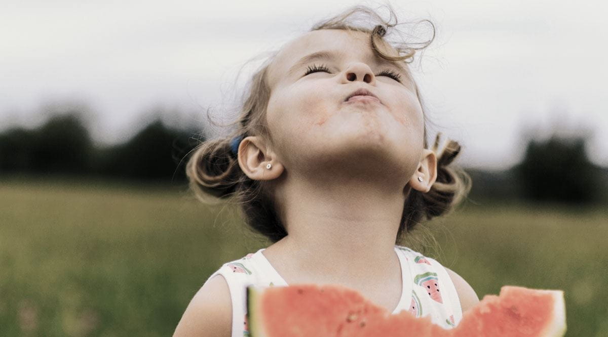 Criança de olhos fechados a desfrutar de uma dentada em fatia de melancia