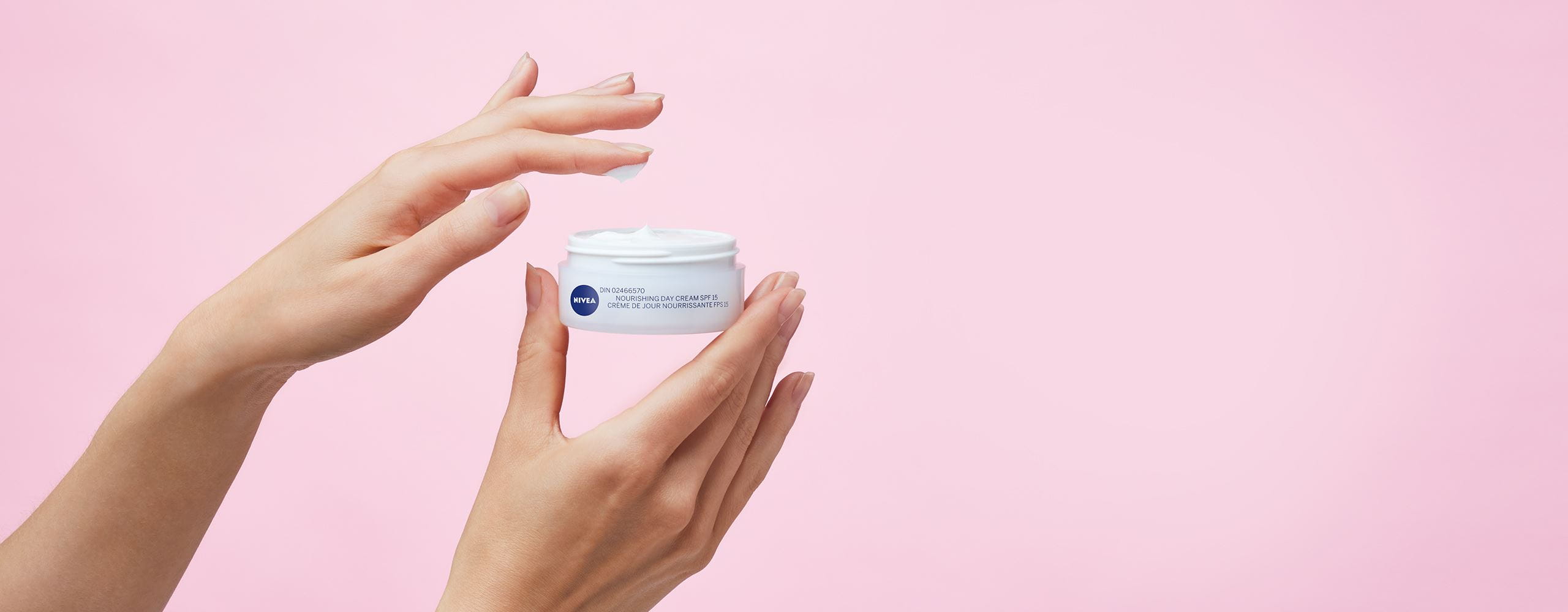 View of Nivea Essentials Nourishing Day Cream SPF15 product held by model on light pink background with product description.