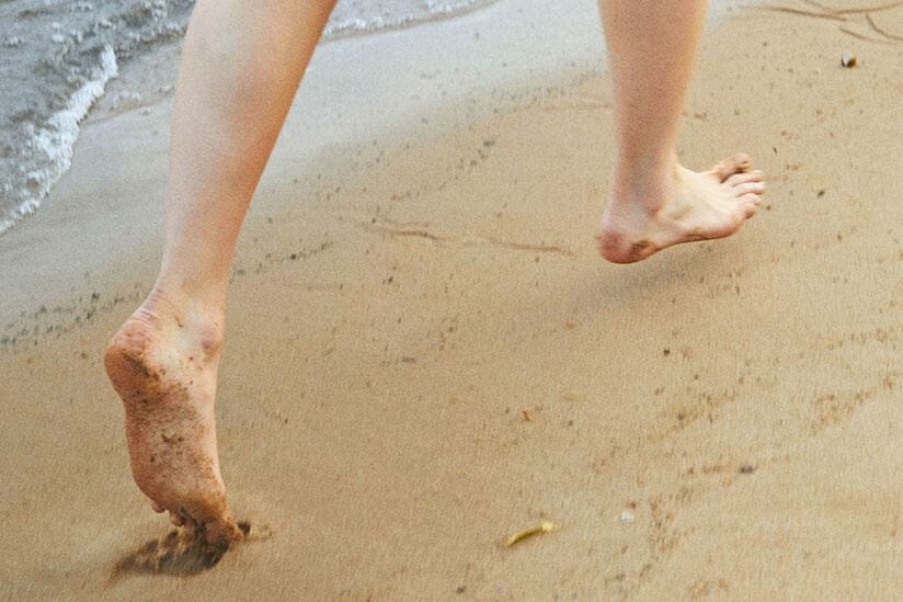 Vue d’une mannequin courant pieds nus sur le sable avec marée d’eau en arrière-plan.