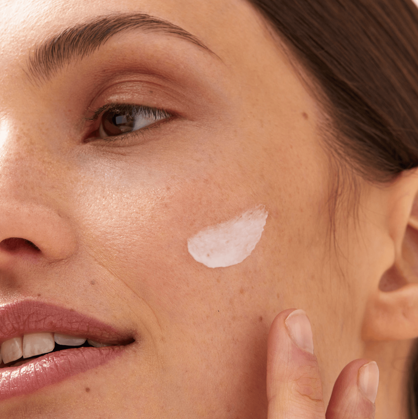 Close up view of a female model with a smudge of Nivea cream on her left cheek.