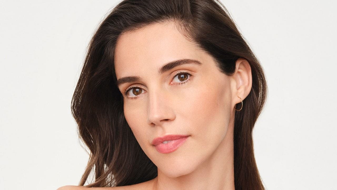 Front view of a model with dark hair and eyes wearing a gold hoop earring against a white background.