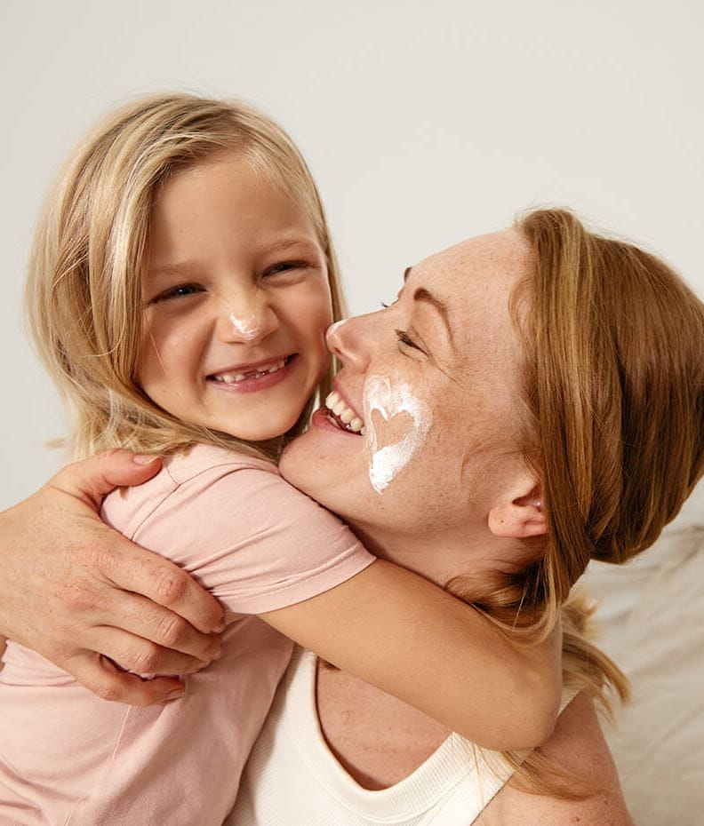 View of a person hugging a toddler with a cream product shown smeared on their face in the shape of a heart.