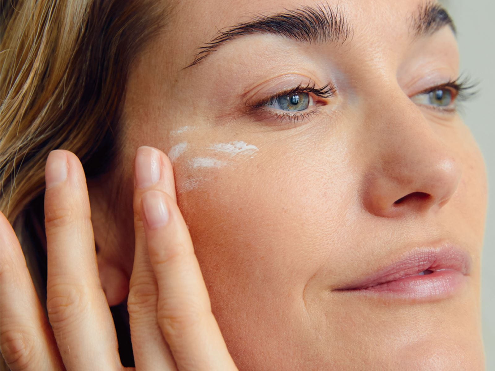 A woman delicately applying moisturizer to her face.
