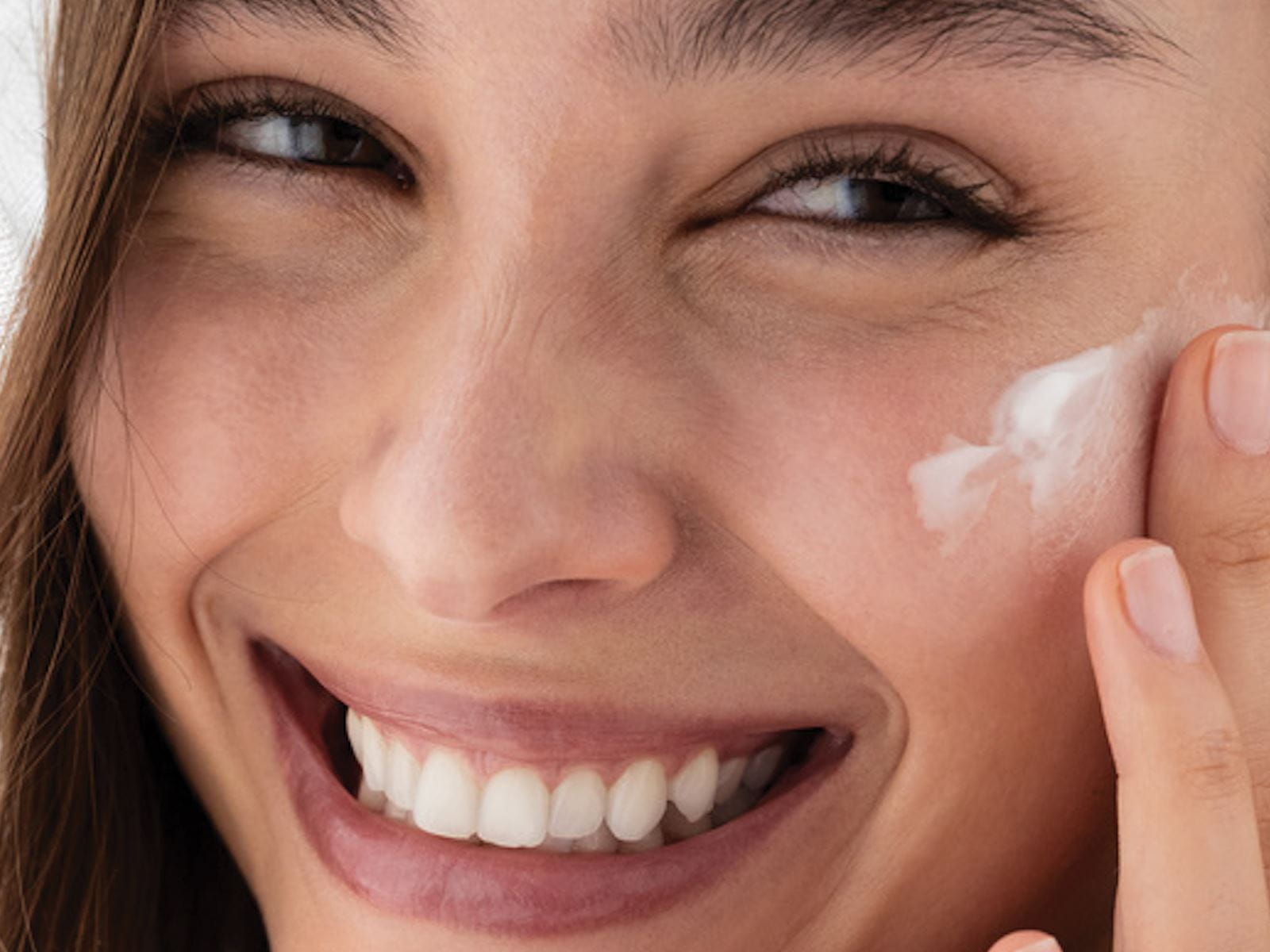 A woman applying cream to her face, her smile radiating contentment.