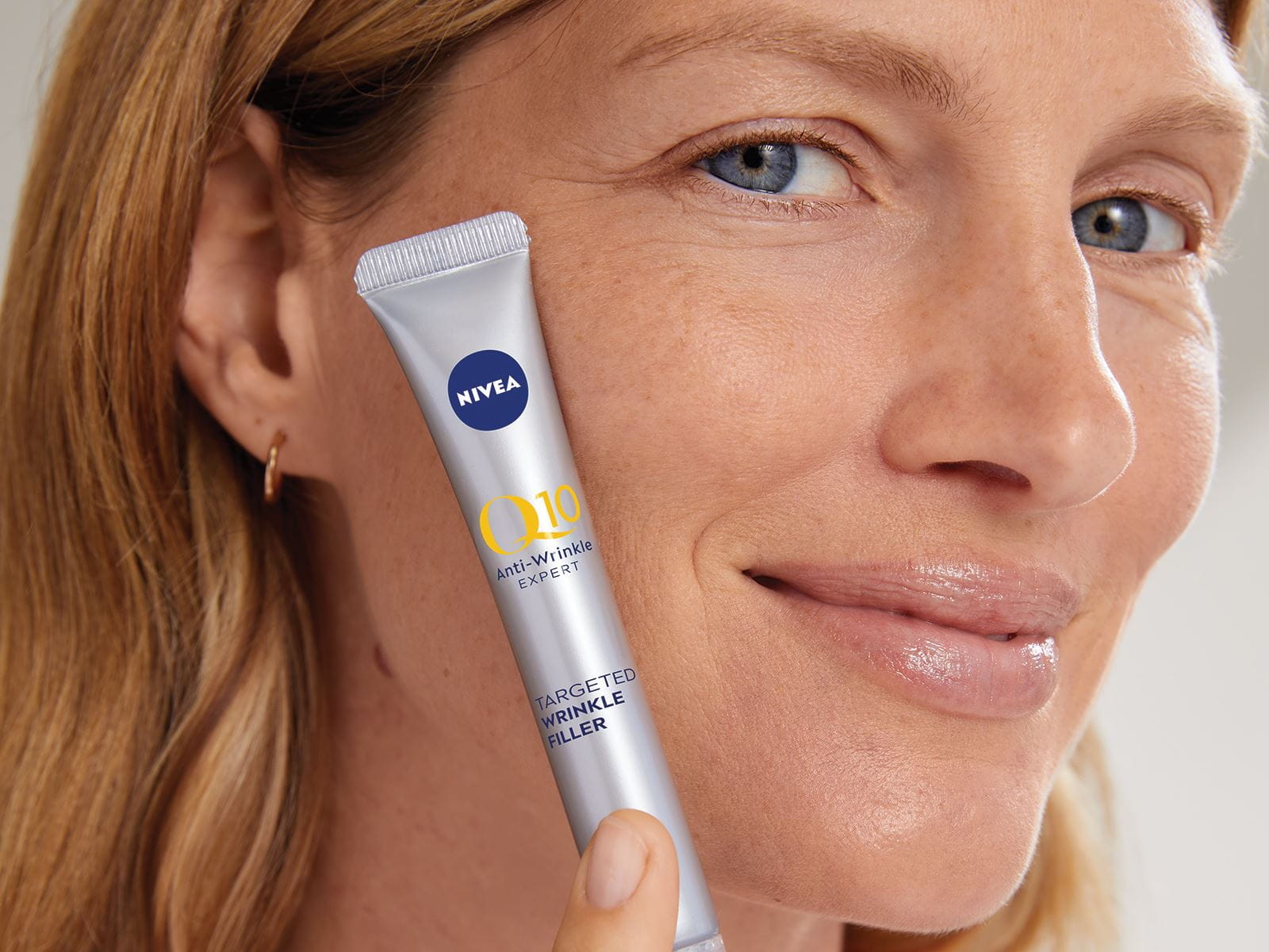 A woman confidently holding a Nivea Q10 product to the side of her face.