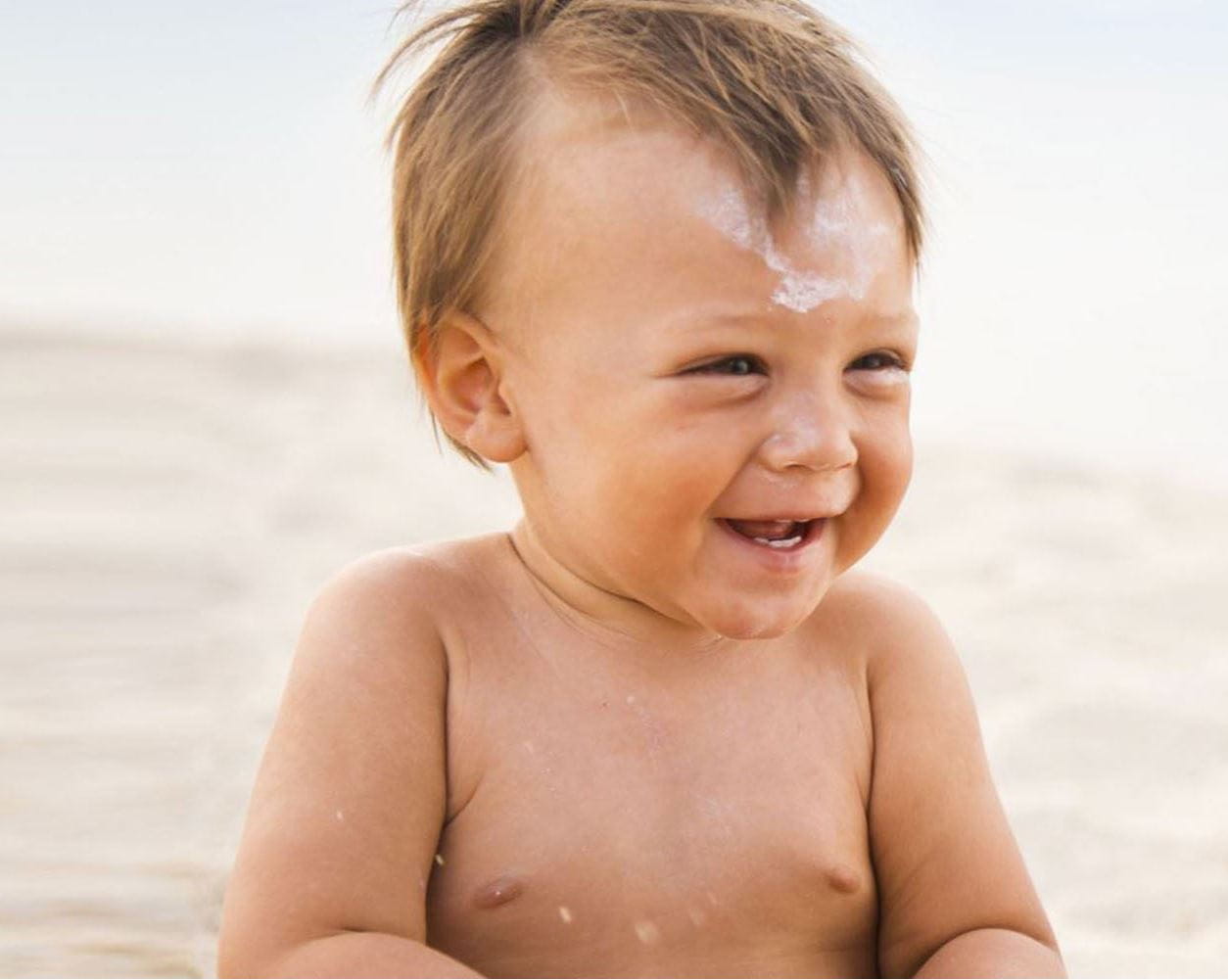 Dítě na pláži s opalovacím krémem