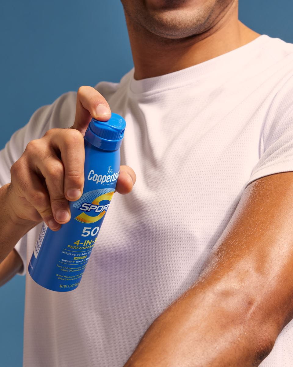 man applying coppertone sport sunscreen spray to his arm