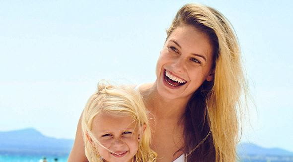 Mujer e hija sonríen en una playa bajo el sol