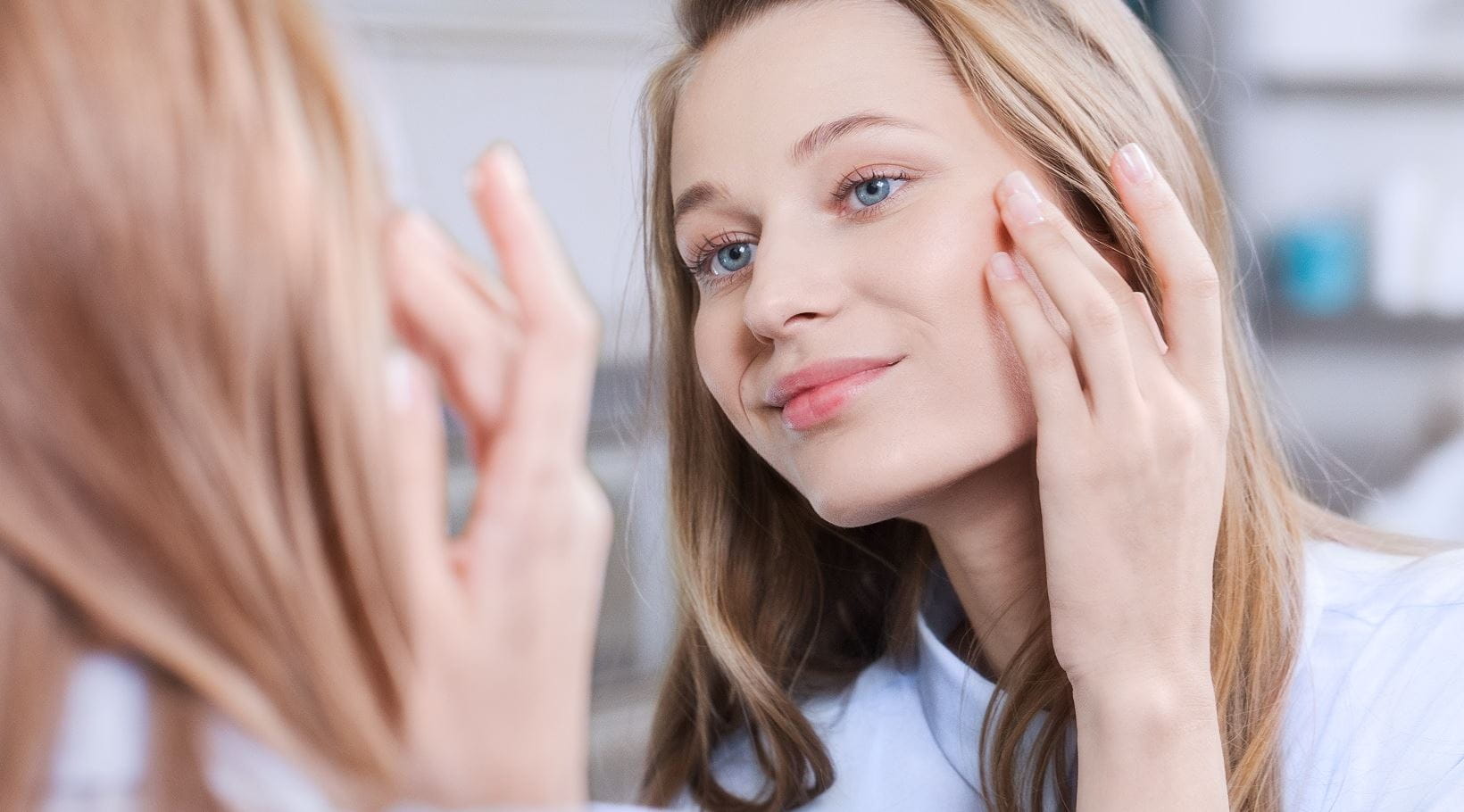 Young woman touching her blotchy cheek in the mirror