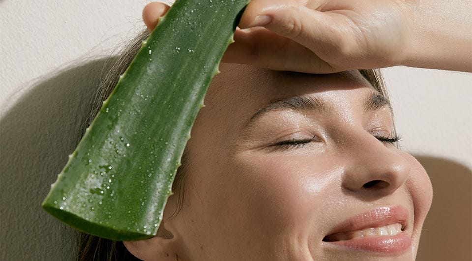 woman smiling and holding an aloe leaf