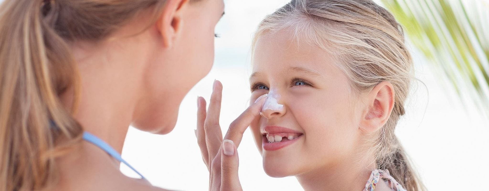 Mother playfully applying sunscreen on her daughter's face