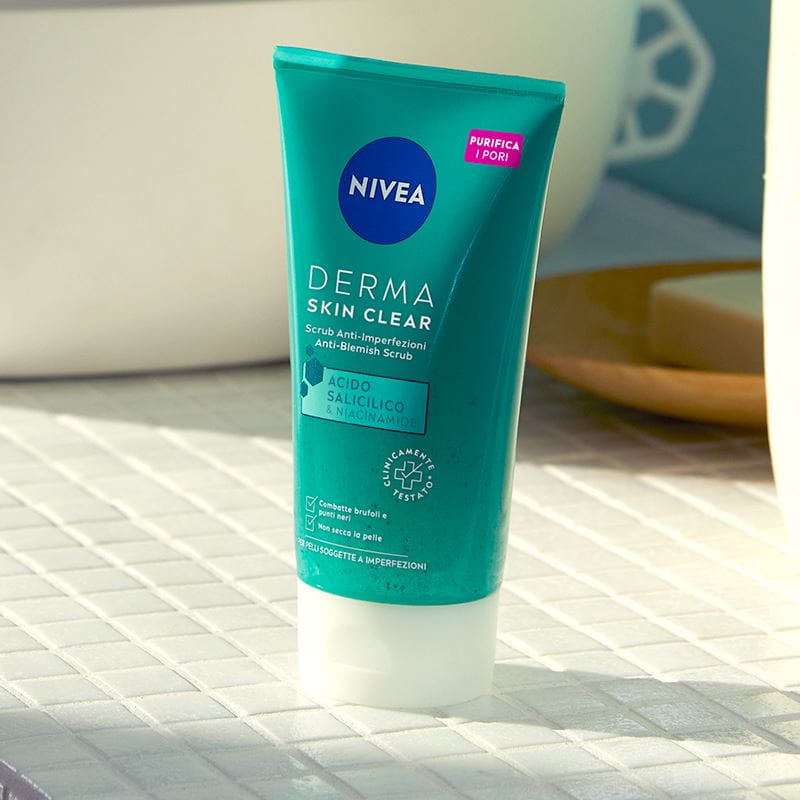 Exfoliante Nivea Skin Clear pousado numa bancada de casa de banho de azulejos junto a um lavatório.