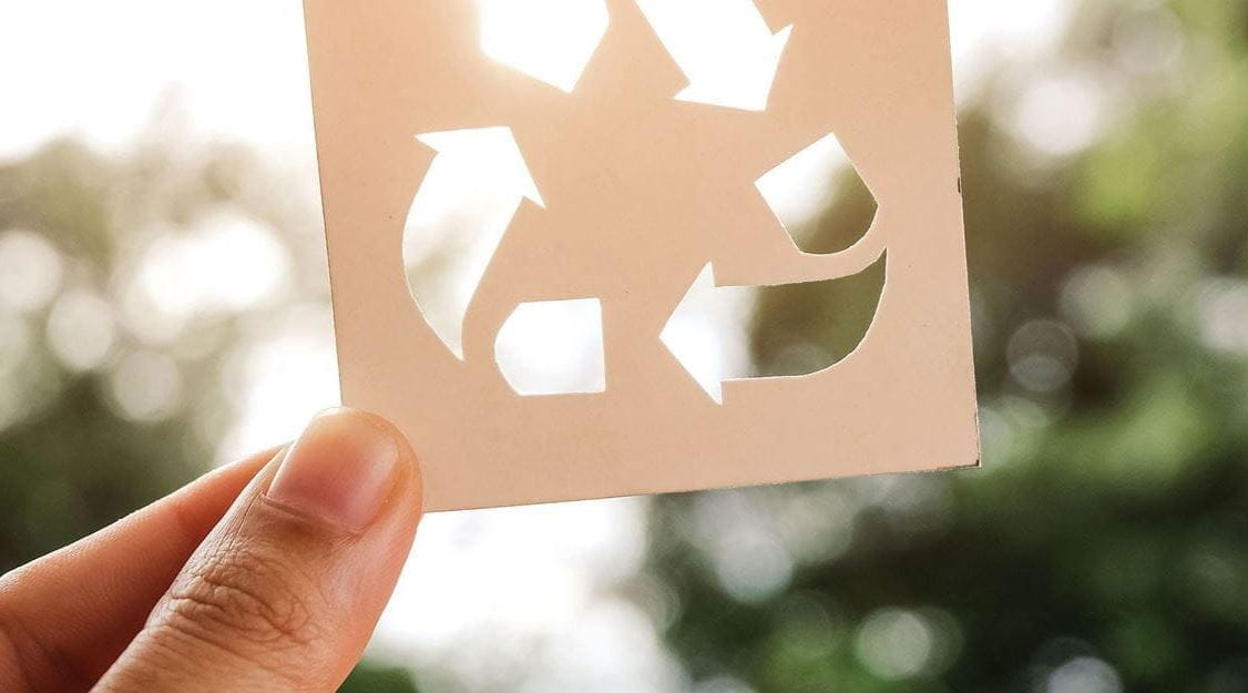 Dedos de pessoa a segurar pedaço de cartão com símbolo de reciclagem.