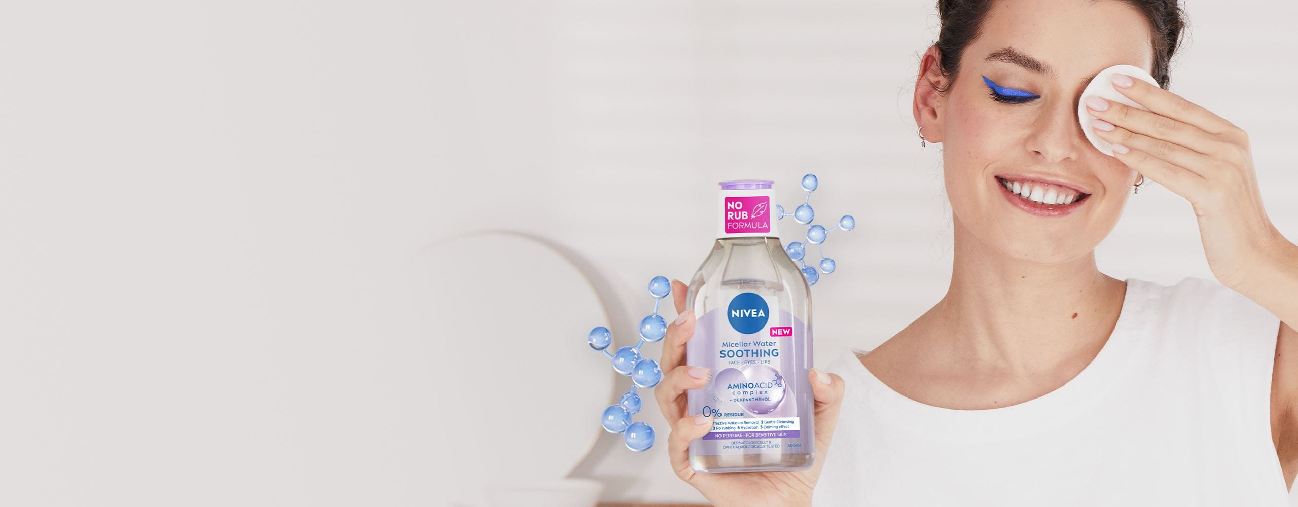 A woman has removed heavy blue eye make-up with the NEW NIVEA Micellar Water and shows the cotton pad. Next to her is the NEW NIVEA Micellar Water package.