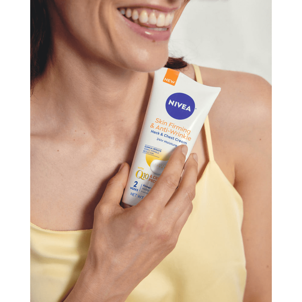 View of a female model smiling while holding up the Nivea Q10 Anti Wrinkle Specialist targeted wrinkle filler product against her chest